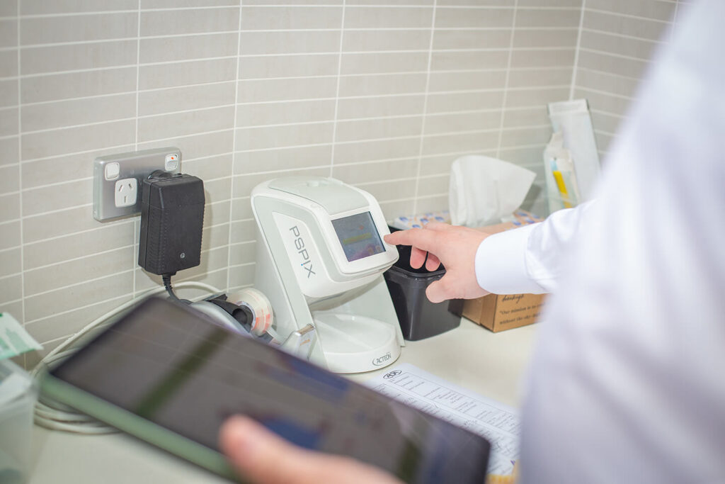 A dental IT support specialist’s hand presses a button on an imaging device in a dental office.