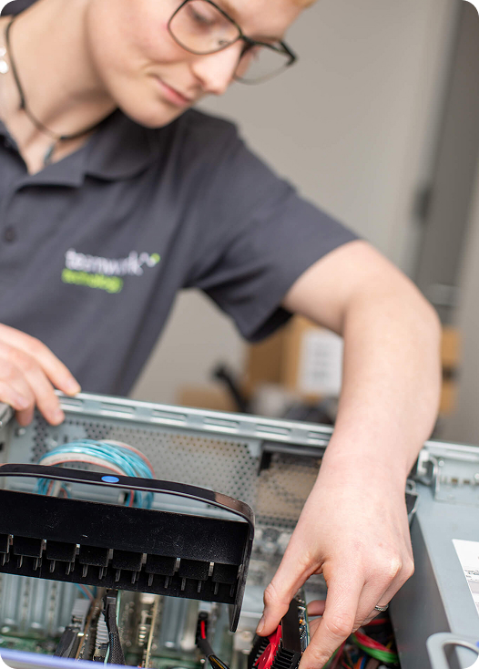 An IT specialist wearing a Teamwork Technology shirt fixes a computer.